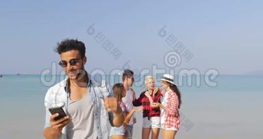 拉丁男子<strong>接听</strong>电话与人们在海滩上的团体在手机上进行视频交谈